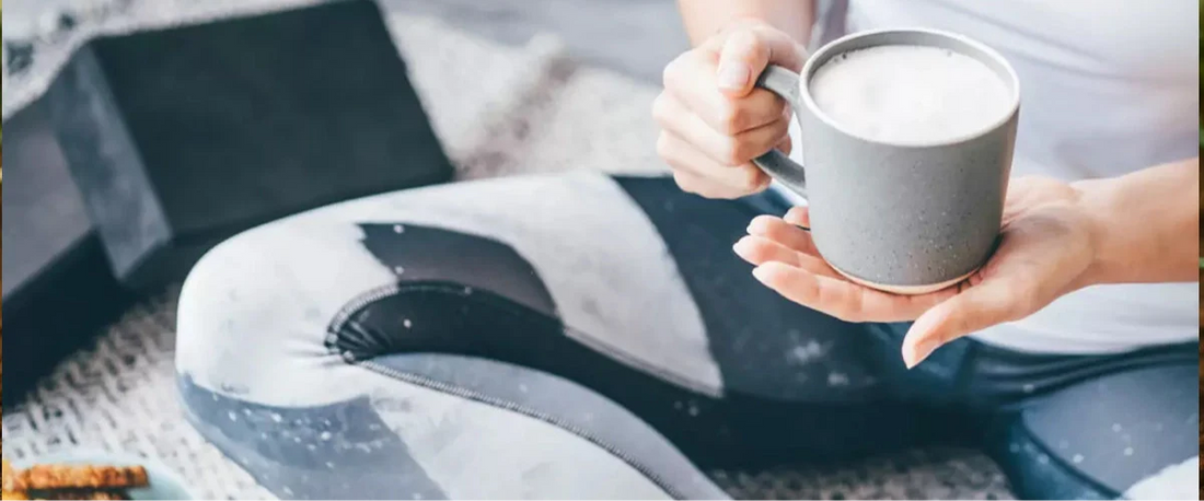 Sportlich gekleidete Frau im Schneidersitz genießt eine Tasse Kaffee nach dem Training.