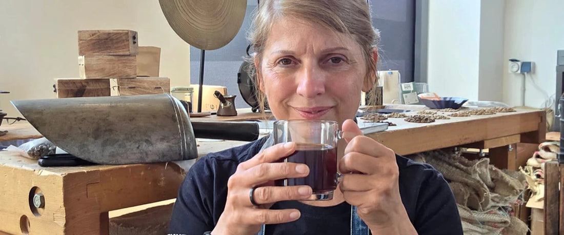 Tina mit Kaffeetasse in der Rösterei, Arbeitstisch im Hintergrund.