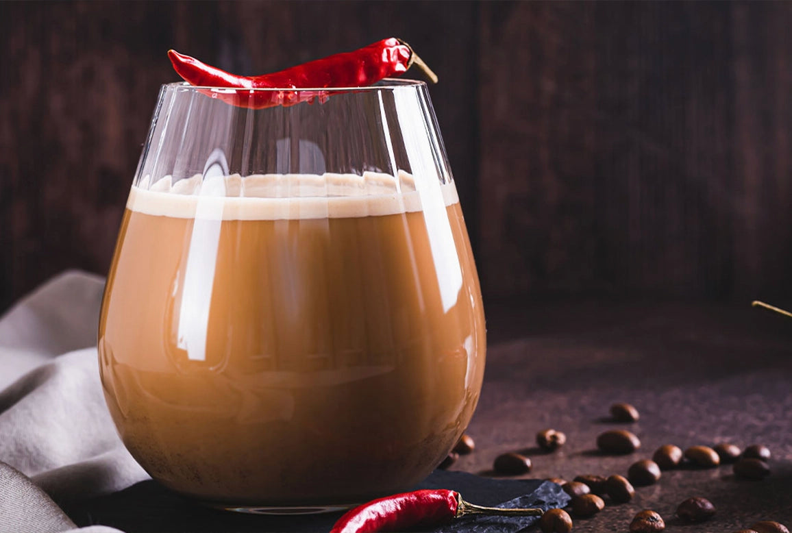 „Glas mit Chili-Kaffee, platziert vor einem schwarzen Hintergrund. Auf dem Glas befindet sich eine feuerrote Chili, die die würzige und pikante Note des Kaffees betont.“