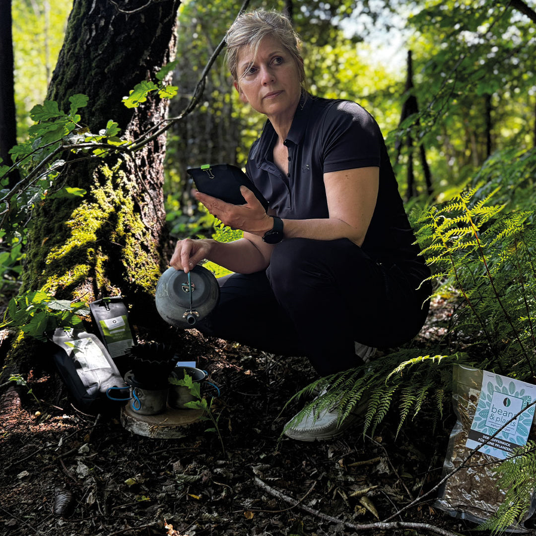 „Tina im Wald, umgeben von der grünen Ruhe der Natur, brüht sich mit einer nostalgischen Kanne ihren Waldkaffee aus der Serie Land- und Waldkaffees auf. Fasziniert von der Umgebung, genießt sie den Moment in vollen Zügen.“