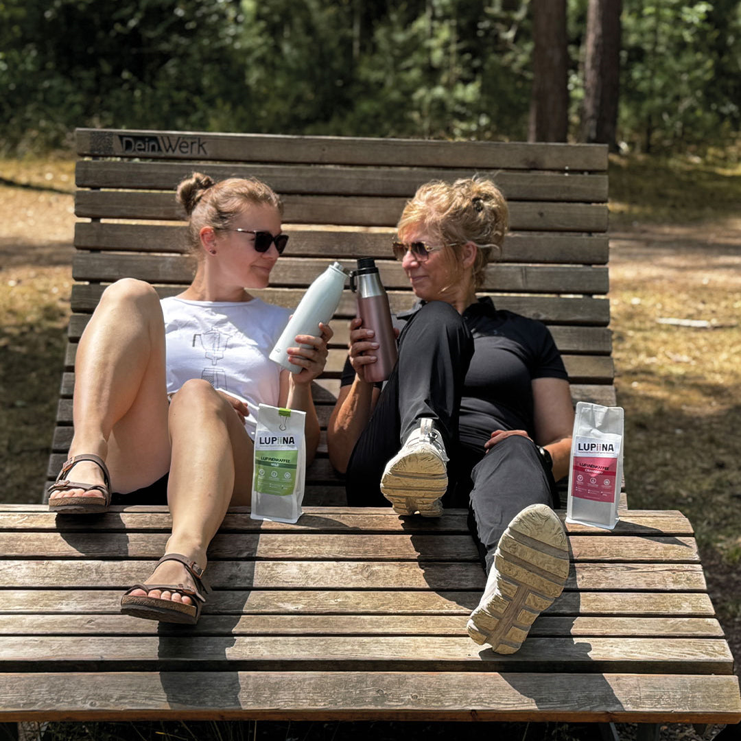 „Lupinenkaffee mild und Cranberry – Nach einer Wanderung in der Teverner Heide stoßen Tina und Sandra auf einer Bank an und freuen sich auf einen kräftigen Schluck ihres jeweiligen Lupinenkaffees aus der ToGo-Flasche.“