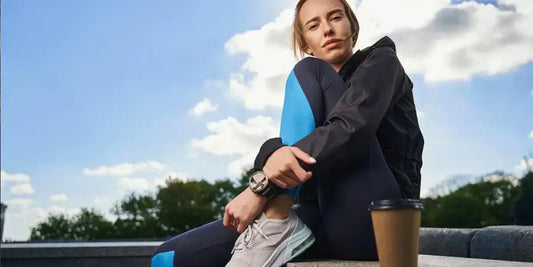 Junge Frau in Sportdress sitzt auf der Mauer, neben ihr ein To-Go-Becher Kaffee – Kaffee und Sport vereint.