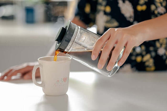 Hand gießt frisch gebrühten Lupinenkaffee aus einer French Press in eine stilvolle Tasse – koffeinfreie Kaffeealternative genießen