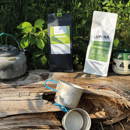 „Im grünen Wald, auf einem alten Baumstamm, präsentieren wir passend zu diesem Naturgrün unsere Sorten Waldmischung Röst-Espressomischung und Lupinenkaffee Lupiina mild. Auf dem Baumstamm, in nostalgischer Stimmung, stehen eine Outdoorkanne und ein Kaffeebecher – perfekt für den Genuss in der Natur.“
