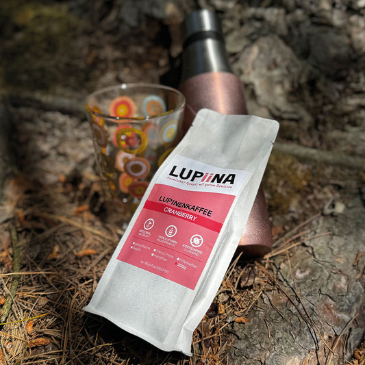 „Lupinenkaffee Lupiina Cranberry, schön drapiert vor passendem Hintergrund. Das bunte Glas und die ToGo-Flasche in Cranberryfarben harmonieren perfekt und verleihen dem Bild trotz des rauen Hintergrunds eine weiche, stimmige Atmosphäre.“
