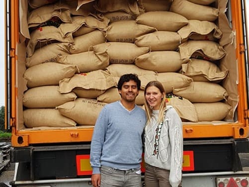 Ein junges Paar eine Deutsche und Peruaner stehen vor einem geöffnetem LKW voller Kaffeesäcke - Fair trade