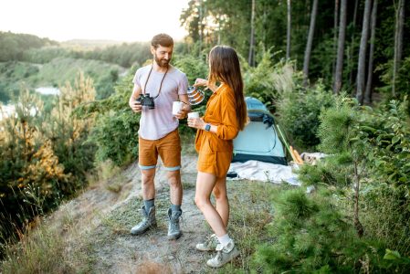 Junges Paar stehen auf einem Campingplatz und genießen ihren Kaffee